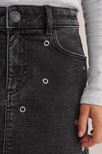 Črna denim krila z srebrnimi očičnimi detajli, zapiranjem na gumb v pasu in skritimi žepi. Teksturirana tkanina z rahlo obrabljenim videzom.