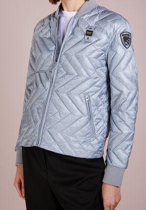 Veste bomber matelassée bleu clair en matériau brillant, dotée d'une fermeture éclair à l'avant, de poches latérales et d'un col côtelé avec écusson logo.