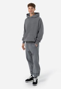 Grauer Kapuzenpullover und passende Jogginghose aus weichem Material. Verfügt über eine Fronttasche, gerippte Ärmelbündchen und ein Logodetail auf der Brust.