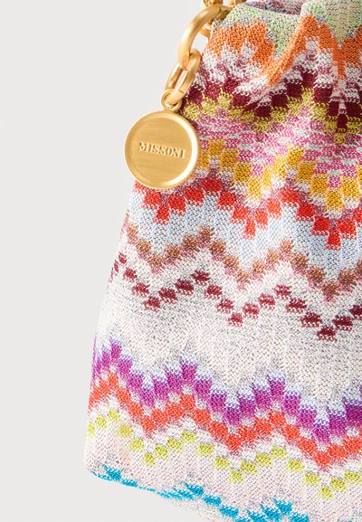 Tissu en maille à motifs zigzag colorés avec une chaîne en or et une étiquette ronde en or gravée du mot "MISSONI" sur un coin de sac à main.