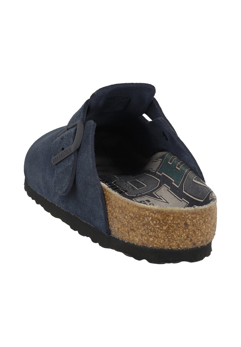 Blauwe suède instapschoen met een kurken voetbed en een getextureerde rubberen zool, met een gemusterde binnenzool die zichtbaar is van achteren.