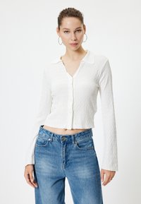 Weißes, strukturiertes Langarmhemd mit Kragen und Knopfverschluss, kombiniert mit hoch taillierten hellblauen Jeans.