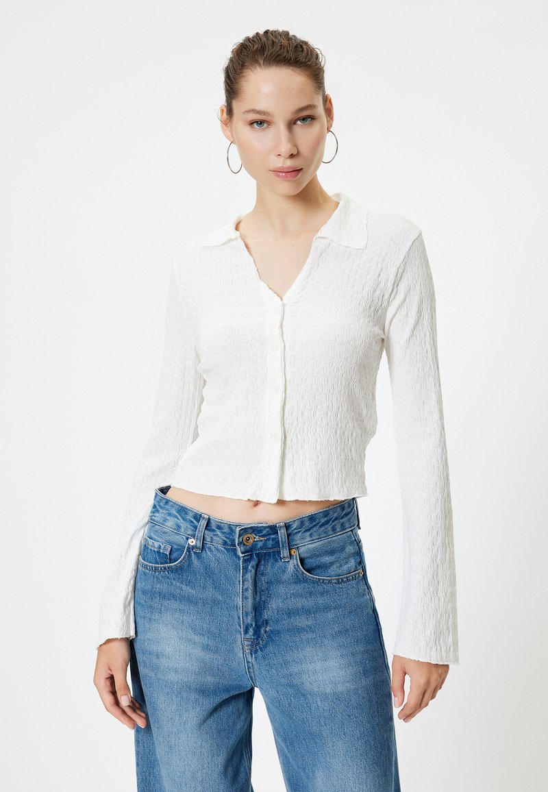 Weißes, strukturiertes Langarmhemd mit Kragen und Knopfverschluss, kombiniert mit hoch taillierten hellblauen Jeans.