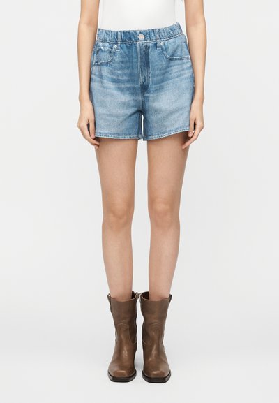 Shorts en denim bleu clair à taille haute, avec un design à cinq poches et une fermeture à boutons. Associés à des bottines en cuir marron.