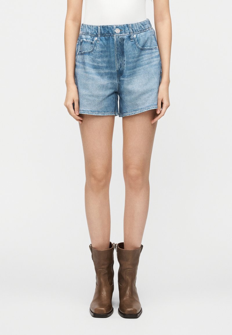 Shorts en denim bleu clair à taille haute, avec un design à cinq poches et une fermeture à boutons. Associés à des bottines en cuir marron.