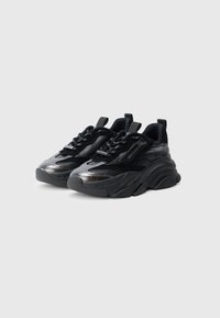 Mustat lenkkarit, joissa on paksu muotoilu, kiiltäviä tekstuuripintoja, verkkokoristeita ja paksut kumipohjat lisäämässä tukea.