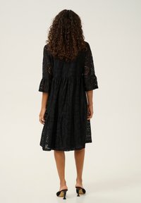 Black lace dress with three-quarter sleeves, flared cuffs, and a tiered skirt. Features intricate patterns and is knee-length.