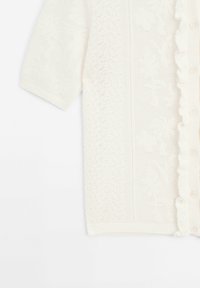 Cardigan blanc en maille à manches courtes avec motifs floraux, bords côtelés et boutons décoratifs le long de l'ouverture devant.