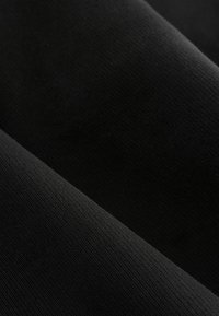 Gros plan sur une texture de tissu côtelé noir montrant un motif fin de tricot et des plis doux.