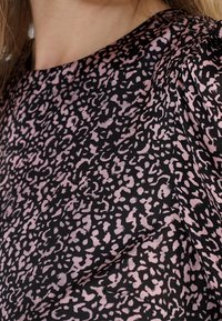 Gros plan sur l'épaule et le cou d'une femme portant un chemisier rose et noir à imprimé léopard avec un col rond.