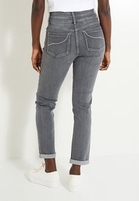 Jeans de mezclilla gris de cintura alta con un acabado texturizado, que presentan puños enrollados y dos bolsillos traseros, combinados con zapatillas deportivas blancas.