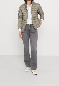 Ljus olivgrön puffjacka med kviltad textur, kombinerad med grå utsvängda jeans och mönstrade vita sneakers, med en knäppt skjorta under.