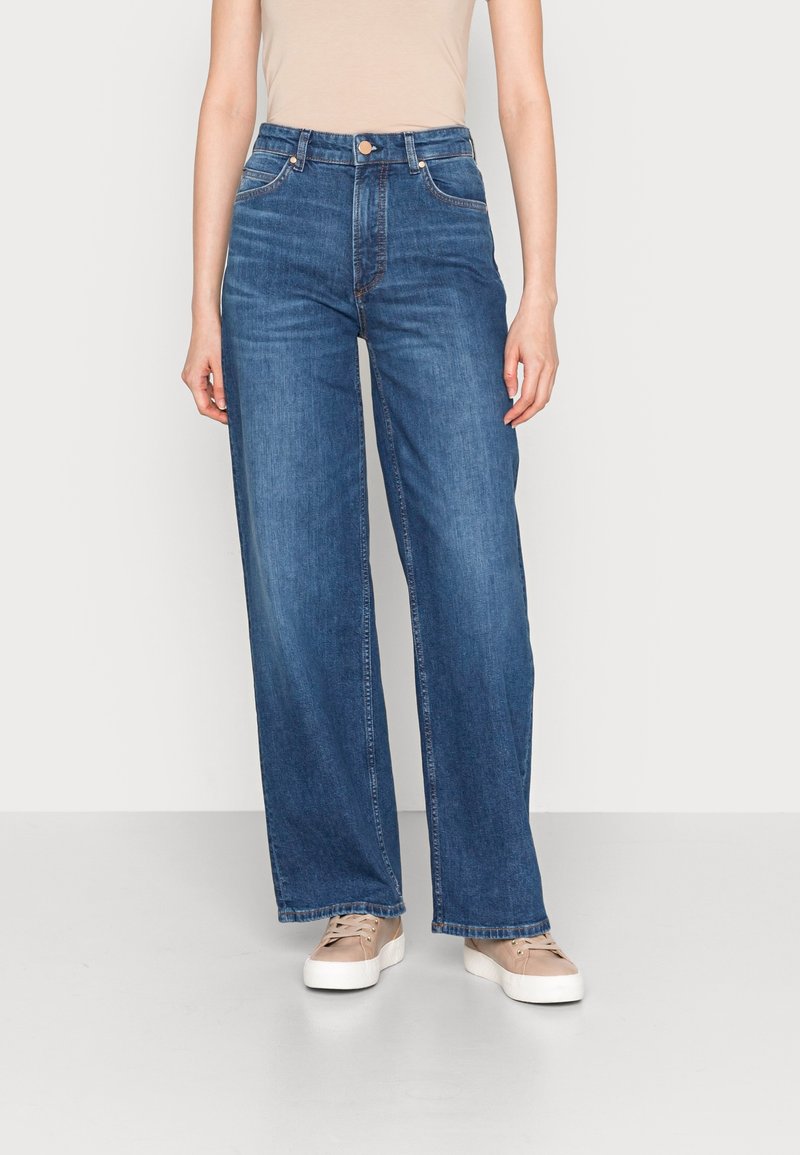 Högmidjade, vida jeans tillverkade av mörkblå denim med en slät yta. Har framfickor och kopparnitar som accent.
