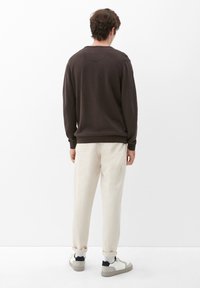 Brauner Strickpullover mit Rundhalsausschnitt, getragen über cremefarbenen, taillierten Hosen und weißen Sneakers mit grauen Akzenten.