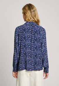 Blusa floreale blu, caratterizzata da maniche lunghe, chiusura con bottoni al collo e una vestibilità morbida. Il motivo include piccoli fiori rosa e bianchi.