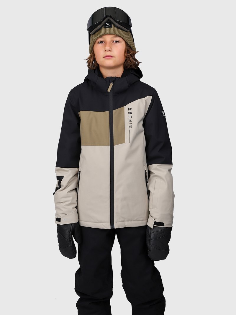 Bambino che indossa una giacca da sci nera, beige e oliva, pantaloni da neve neri, muffole nere, un cappello oliva e occhiali da sci in testa su uno sfondo grigio.