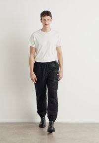 Schwarze, leichte Hose mit elastischem Bund; strukturierter Stoff; schmal zulaufende Beine; kombiniert mit einem schlichten weißen T-Shirt und schwarzen Stiefeln.