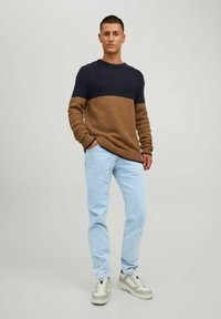 Pull en tricot avec une partie supérieure marine et une partie inférieure marron, motif texturé, encolure ronde, associé à un jean bleu clair et des baskets.