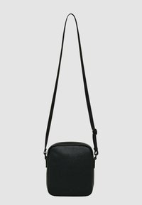 Borsa a tracolla nera in pelle testurizzata. Presenta una forma quadrata, tracolla regolabile e chiusura con cerniera. Design minimalista senza elementi metallici visibili.