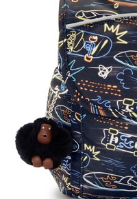 Rucksack aus schwarzem Stoff mit einem bunten, skateboard-inspirierten Druck. An ihm hängt ein fluffiger schwarzer Gorilluschlüsselanhänger mit braunen Akzenten.