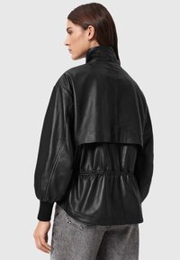 Μαύρο δερμάτινο μπουφάν με ψηλό γιακά, φουσκωτά μανίκια και σφικτή μέση. Λείο υλικό με κοντό σχέδιο και ελάχιστα μεταλλικά στοιχεία.