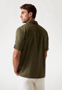 Chemise à manches courtes, à boutons, de couleur vert olive avec un motif en losanges et des accents de design subtils. Dotée d'un col classique et d'une coupe décontractée.
