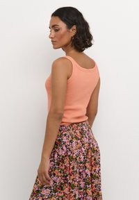 Débardeur pêche avec un décolleté dégagé, assorti à une jupe à motif floral aux teintes roses et vertes, froncée à la taille.