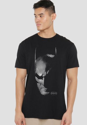 Young man wearing a black t-shirt featuring a stylized Batman face design with diagonal lines and a small Batman logo.