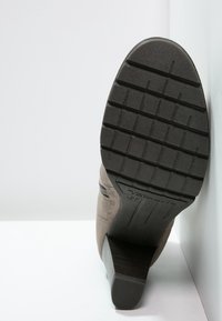 Brun mockaimitation ankelstövel med en klack, strukturerad gummisula och sömnadsdetaljer. Sulan har ett mönstrat grepp för bättre fäste.