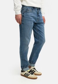 Lyseblå denimjeans med avslappet passform, oppbrettede nederkanter og subtil fading. Kombinert med beige og svarte sneakers med lav topp.