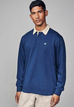 Navy long-sleeve polo shirt with a beige collar, featuring a front placket and embroidered logo on the left chest. Cotton blend fabric.