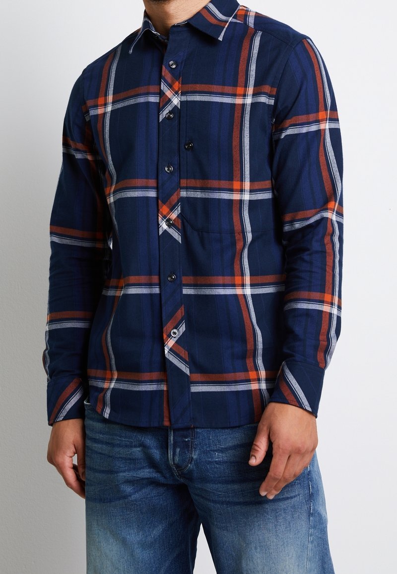 Marinblå och orange rutiga långärmade skjorta med knappkrage, texturerad tyg och en bröstficka.