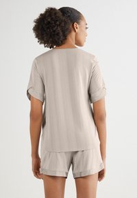 Beige top s krátkým rukávem s vertikálními pruhy a ohrnutými manžetami, zkombinovaný s odpovídajícími šortkami se uvolněným střihem a jemným leskem.