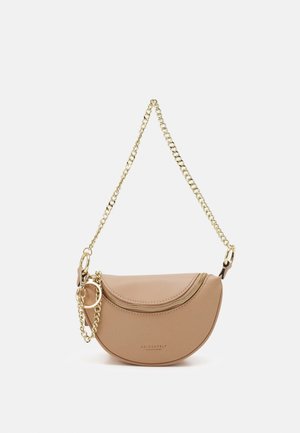 Sac bandoulière beige en forme de demi-lune avec une sangle chaîne dorée, une fermeture éclair dorée et un petit anneau doré sur fond uni.