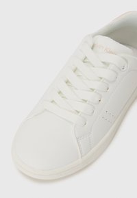 Baskets blanches en cuir lisse avec un bout rond, des lacets plats et de légères perforations sur le côté. Nom de la marque embossé sur la languette.