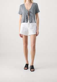 Top corto de cuadro vichy en blanco y negro con escote en V y cierre con lazo, combinado con pantalones cortos de denim blanco con bordes deshilachados y zapatos de slip-on negros.