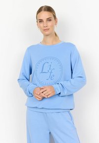 Világoskék pulóver, amely puha anyagból készült, kör alakú nyakkivágással és grafikus szövegformázással az elején, kör alakú mintában.