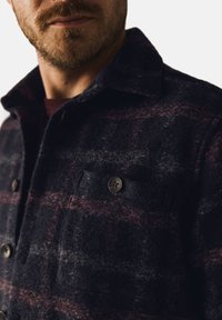 Wollen blended jas met een donker marineblauw en bordeaux geruit patroon, met een knoopsluiting aan de voorkant en borstzakken. Geweven stof.