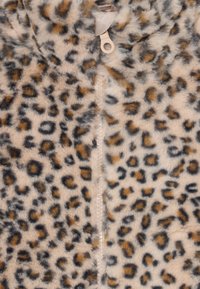 Fleece mit Leopardenmuster, das eine weiche Textur, beige und braune Farbgebung sowie einen zentralen Reißverschluss mit einem runden Zugring aufweist.