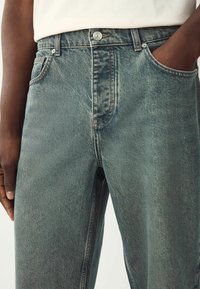 Jean en denim bleu clair avec une coupe droite, présentant une fermeture à bouton, cinq poches et une texture légèrement délavée.