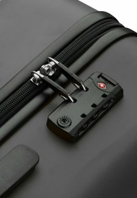 Black hard-shell suitcase detail featuring a textured finish, waterproof zipper, and a combination lock with a red accent.