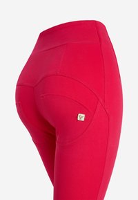 Mallas rojas hechas de tejido elástico, con una cintura alta, detalles de costura curva, y un pequeño logo cerca de la cadera.