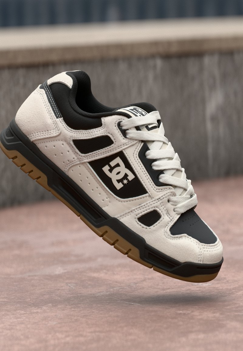White and black skate shoes feature a synthetic upper, rubber sole, perforated accents, and prominent logo with a gum outsole.
