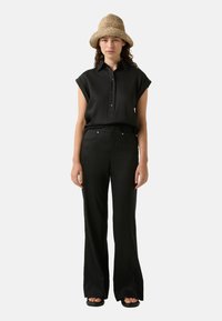 Zwarte korte mouwen shirt met kraag en knopenlijst, gecombineerd met hoog draagt zwarte wijde broek. Geweven strohoed maakt de outfit compleet.
