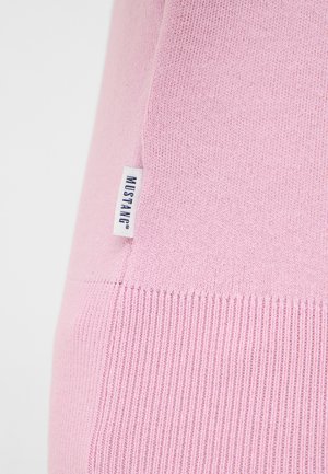 Helles rosa Strickpullover mit geripptem Muster, versehen mit einem Seitenschild, auf dem "MUSTANG" steht. Glattes Material mit körpernahem Schnitt und klaren Linien.