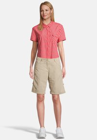 Rot-weiß karierte Kurzarmbluse mit Kragen, kombiniert mit beigen Knielangen Shorts. Weiße Sneakers runden das Outfit ab.