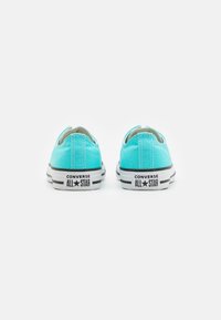 Zapatillas de lona turquesa con suelas de goma blanca. Presenta un logo y rayas negras. Diseño de corte bajo con punta redondeada y tirador en la parte posterior.