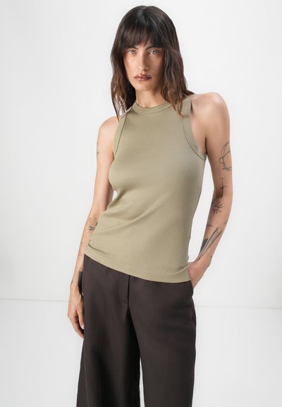 Top sin mangas de canalé en verde oliva con cuello alto. Combinado con pantalones anchos de color marrón oscuro. Textura suave, estilo ajustado.