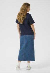 T-shirt en coton navy associé à une longue jupe en denim. La jupe présente une coupe droite et des poches arrière, portée avec des baskets blanches et des chaussettes.