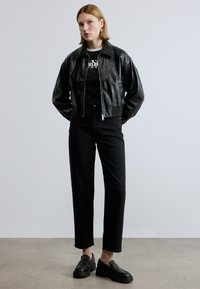 Μαύρο δερμάτινο μπουφάν με κοντό σχεδιασμό, κλείσιμο με φερμουάρ, δύο πλαϊνές τσέπες, συνδυασμένο με μαύρο κοντομάνικο πουκάμισο, μαύρο παντελόνι ψηλής μέσης και μαύρα παπούτσια.